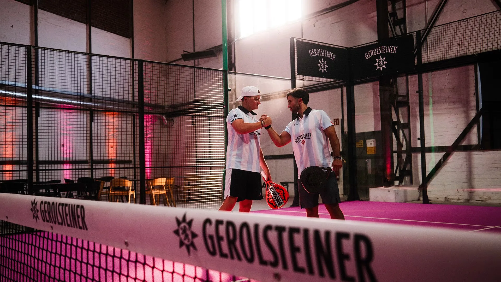 Zwei Padel-Spieler geben sich die Faust auf einem magenta Court, Gerolsteiner am Netz
